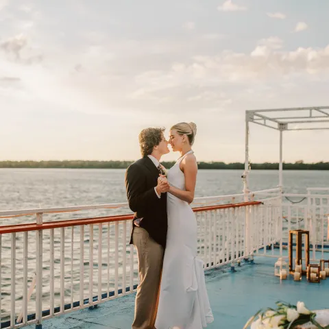 Couple embracing on a boat deck at sunset, with a scenic water view.