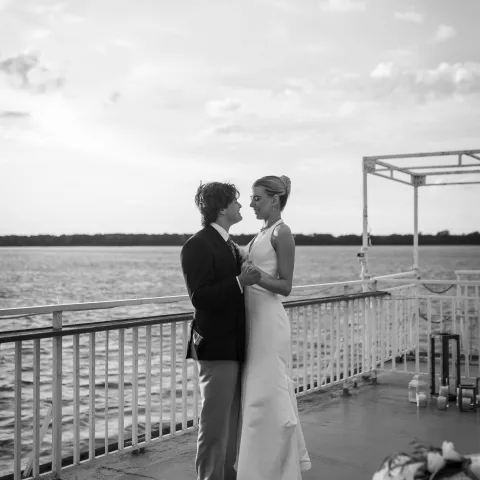 Couple in wedding attire dancing on a boat deck at sunset.