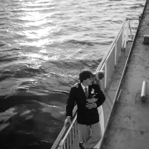 Couple standing on a ship deck, embracing, with ocean in the background, in black and white.