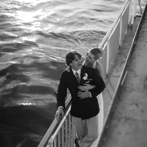 Bride hugging groom on a dock by water, black and white photo.