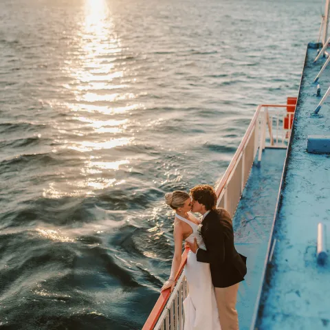 Couple embracing on a boat deck at sunset over the water.