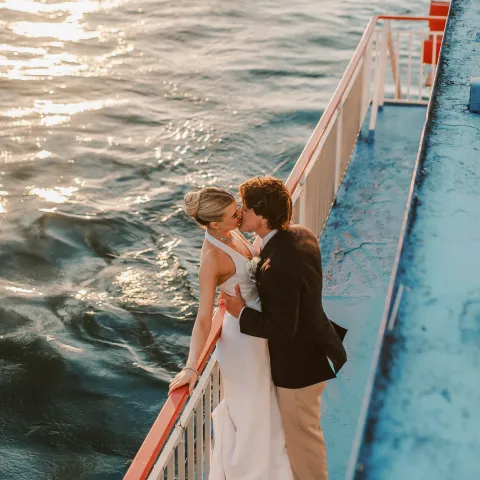 Couple embracing on a boat deck at sunset over the water.