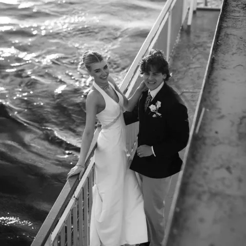Couple in formal attire smiling by the water on a sunny day.