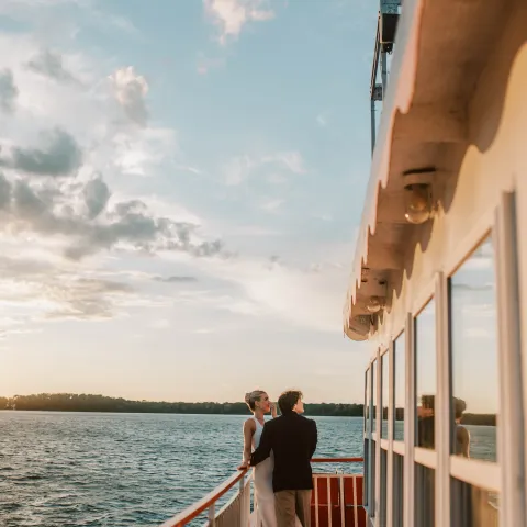 Couple standing on a boat deck at sunset with water and sky in the background.