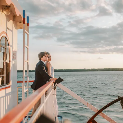 Couple embracing on a boat at sunset with clouds and water.