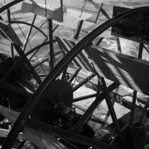 Black and white photo of a paddle wheel on a boat, with water splashing.