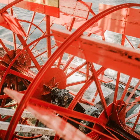 Red paddle wheels of a riverboat against the water.