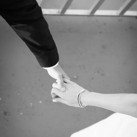 Black and white photo of a couple holding hands on a bridge.