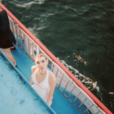 Woman in white dress looking up from a boat on the water.