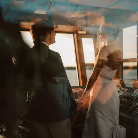 Couple in wedding attire on a boat with reflections on the glass.