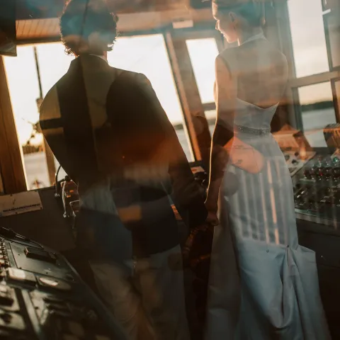 Couple in formal attire in boat cabin at sunset.
