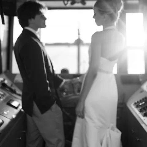 Black and white photo of a couple in formal attire, standing in a ship's control room.