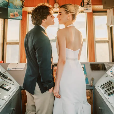 Couple in formal attire standing in a ship's control room, smiling at each other.