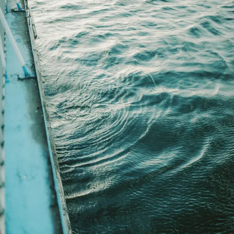 Side of a boat with metal railing and rippling water surface.