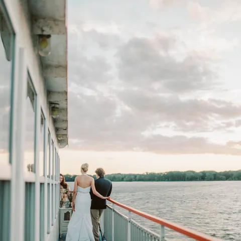 Couple in formal wear on boat deck at sunset.