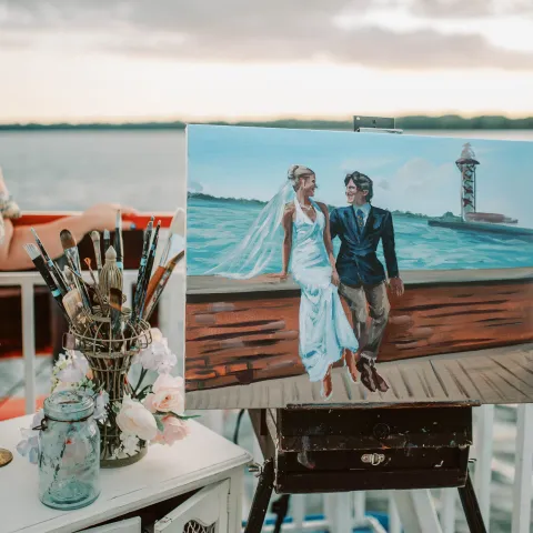Artist on a boat with painting of a bride and groom by the sea