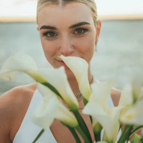 Woman with bouquet of calla lilies in front of her face, smiling.