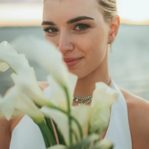Woman smiling, holding white flowers by a body of water.