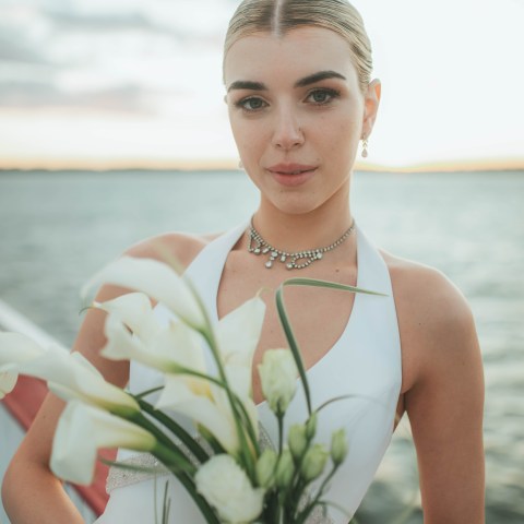 Woman in white dress holding white flowers by the water.
