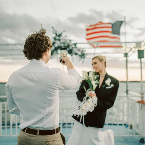 Man taking photo of woman on boat deck with American flag in background.