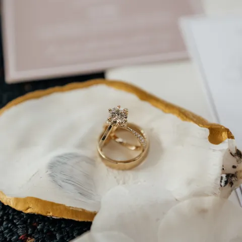 Two gold rings on a shell with gold rim, placed on floral fabric.