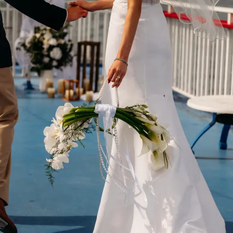 Bride in white gown holding calla lilies bouquet on a boat deck.