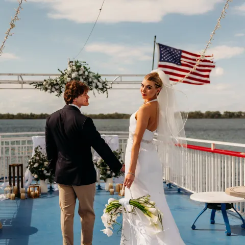 Bride and groom on boat deck with floral decor and U.S. flag.