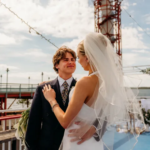 Bride and groom embracing outdoors, tower in background.