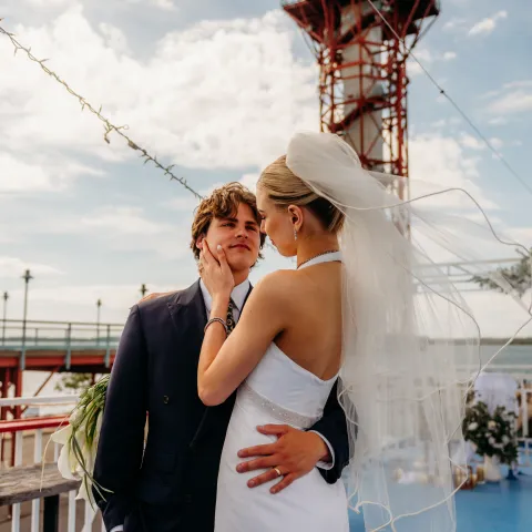 Bride and groom embrace on a boat deck under a blue sky.