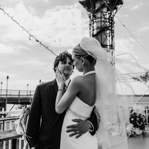 Bride and groom embracing on a dock under string lights.