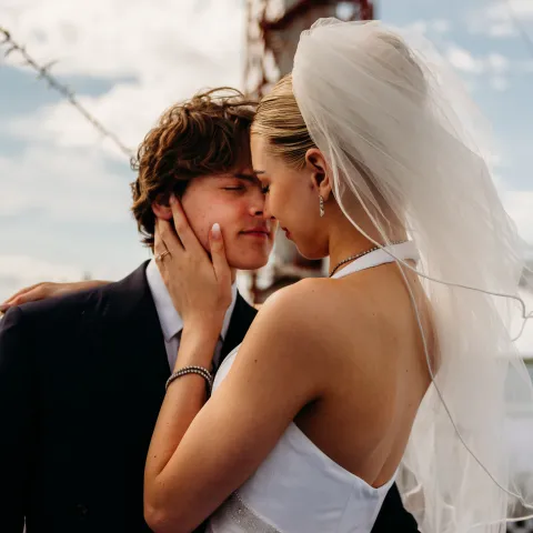 Bride and groom embrace outdoors under a cloudy sky.