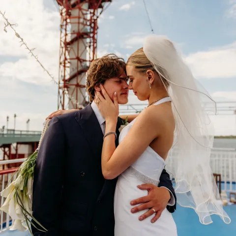 Bride and groom embrace on a boat deck with a lighthouse in the background.