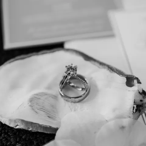 Black and white photo of wedding rings on a shell with blurred background.