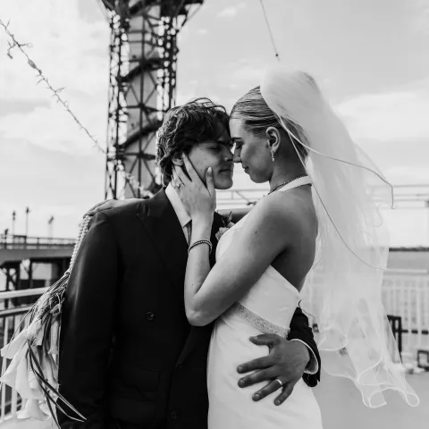 Bride and groom embrace near a tower structure, her veil flowing.