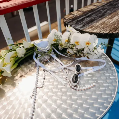 Sunglasses, pearl necklace, and white flowers on a metal table.