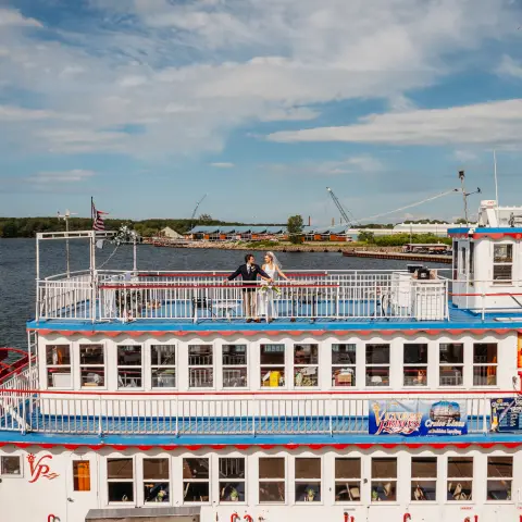 Riverboat with people on top deck against a lake and blue sky.