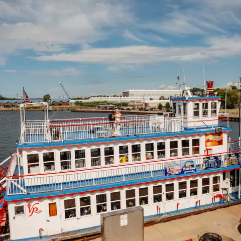 Colorful riverboat docked beside a river, clear sky with scattered clouds.