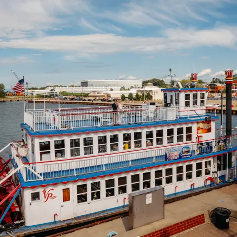 A vintage riverboat docked by a riverbank under a blue sky.