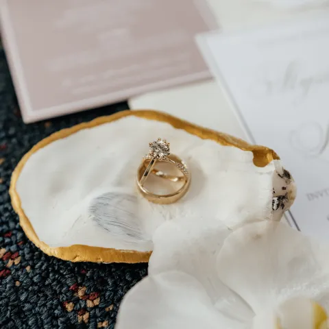 Gold ring on fabric with floral detail and blurred papers in background.