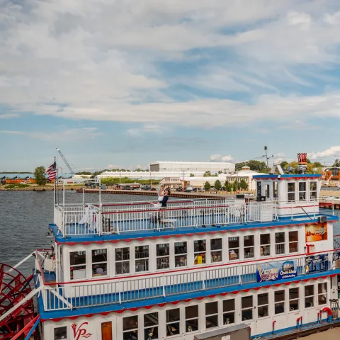 A vintage-style riverboat docked by the riverside under a partly cloudy sky.