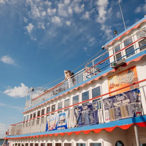 Side view of a multi-deck boat with banners, under a clear blue sky.