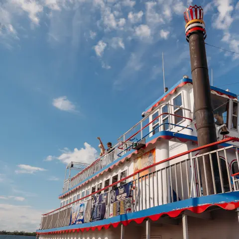 People on a riverboat with red and blue trim under a blue sky.
