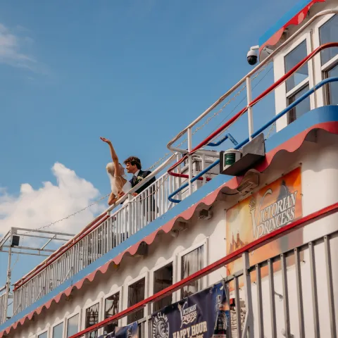 People on a decorated boat deck with posters, against a blue sky.