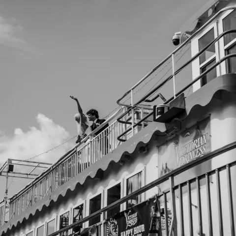 Black and white image of a person waving from a boat deck.