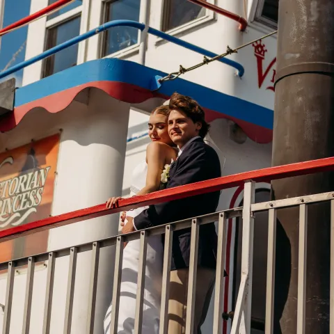 Couple in wedding attire stands on a boat deck.