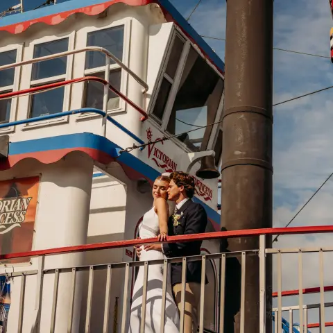 Wedding couple kissing on a boat deck with a bright, cloudy sky.