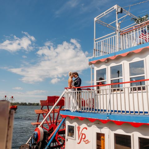 Couple embraces on white riverboat under blue sky with clouds.