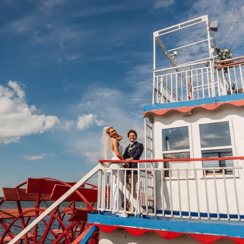 Bride and groom on a paddleboat with a blue sky backdrop.