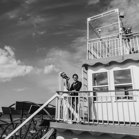 Bride and groom on paddle steamer stairs, with cloudy sky.