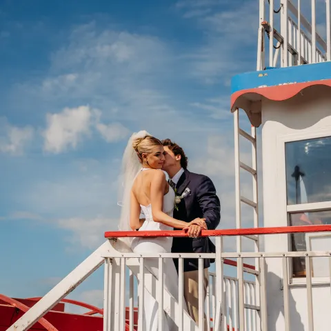 Bride and groom kissing on a boat deck under a blue sky.
